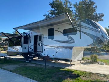 White and gray RV with extended awnings parked.