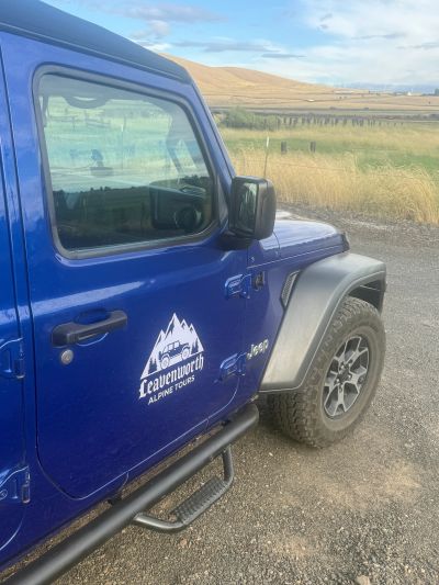 Blue Jeep with Leavenworth Alpine Tours logo in rural area.