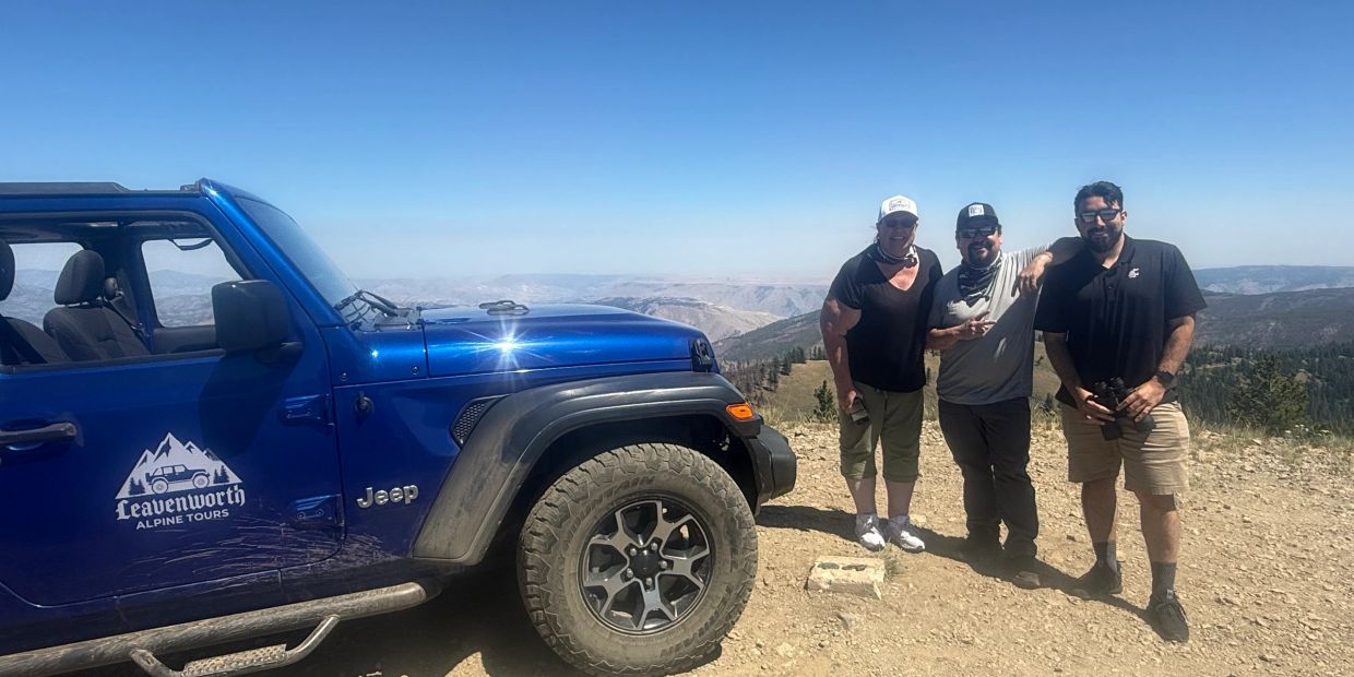 Three guests standing beside a blue Jeep at a scenic mountain viewpoint near Chumstick Peak.
