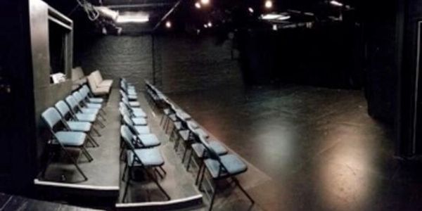 Empty small theater with blue chairs and dark stage.