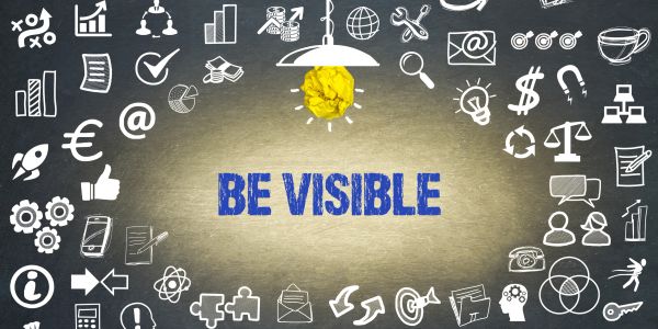 Text "BE VISIBLE" illuminated by a hanging light surrounded by business icons.