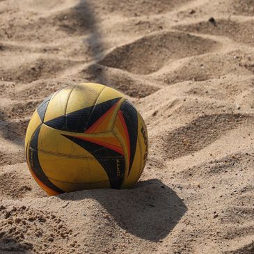 Yellow and black volleyball resting on sandy beach.
