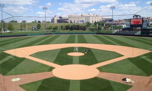 Empty baseball field with three people near the pitcher's mound on a sunny day.