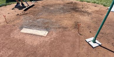 Baseball pitcher's mound being maintained with tools on a sunny day.