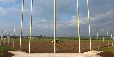 Construction site with metal poles and a tractor on a dirt field under a cloudy sky.