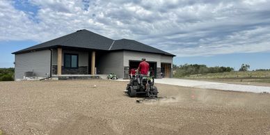 Person using a tractor to prepare soil in front of a modern house.