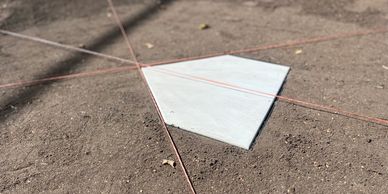 A pentagonal home plate on a dirt field with intersecting orange guide strings.