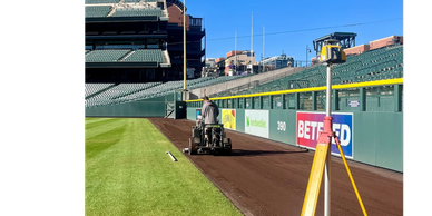 A person operating groundskeeping equipment on a baseball field's dirt track.