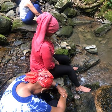 Three women sitting by a rocky stream with feet in the water.