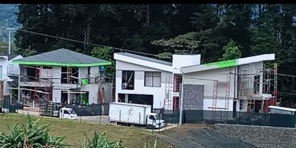 Two modern houses under construction with scaffolding and trucks outside.