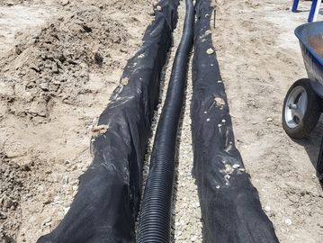 Black drainage pipe installed in a gravel trench at a construction site.