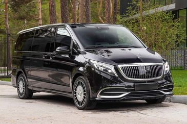 Luxury black van parked on a street near trees and a building.