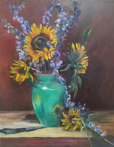 Sunflowers and purple flowers in a green vase on wooden table.