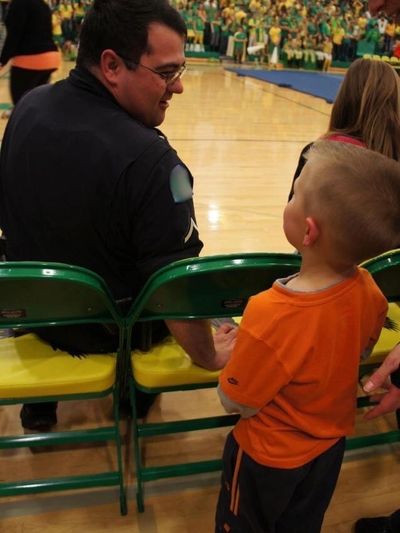 A police officer holding hands with a young boy in a gymnasium.