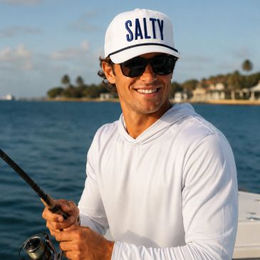 Man fishing on a boat wearing a white "SALTY" cap and sunglasses.