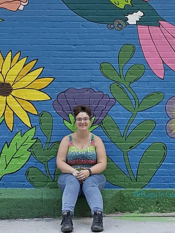 a photo of Katie with a colorful painted brick background