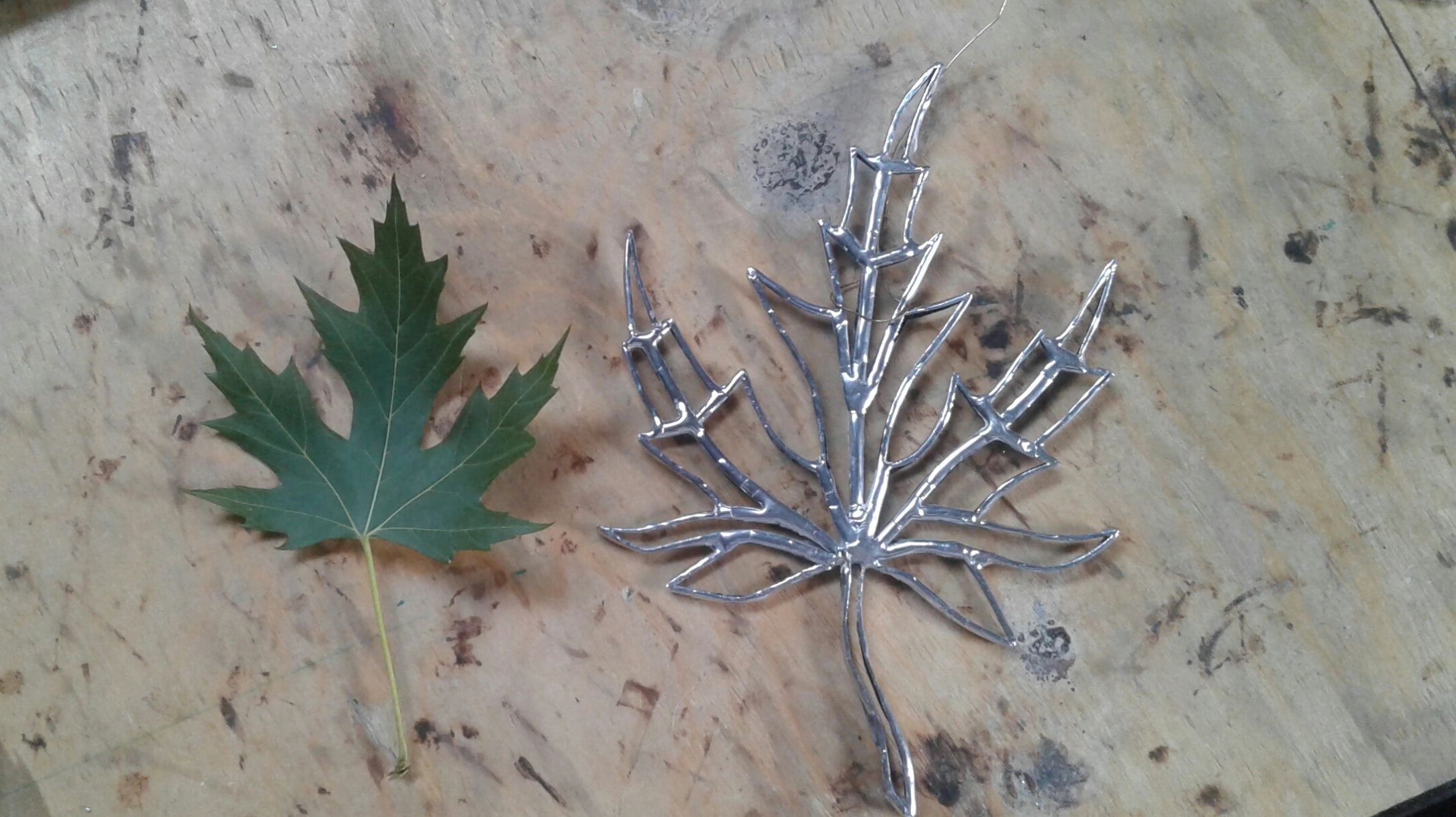 A clear glass maple leaf next to a real maple leaf