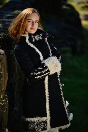 Woman in a black fur-trimmed coat leaning against a stone wall.