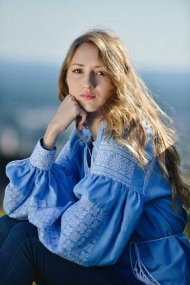 Young woman with long blonde hair in a blue embroidered blouse.