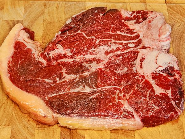 Raw ribeye steak on a wooden cutting board.