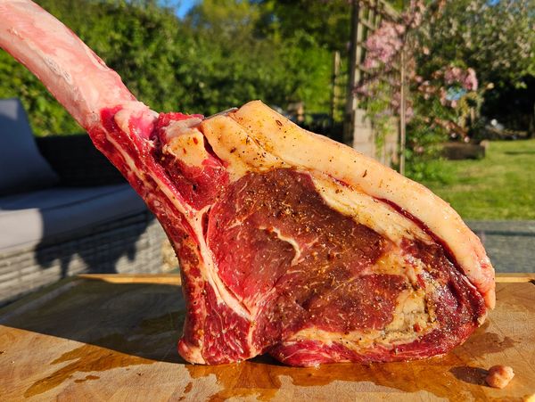 Raw tomahawk steak on a wooden cutting board outdoors.