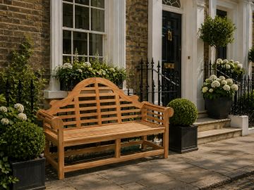 A wooden bench outside a brick house with potted greenery and flowers.