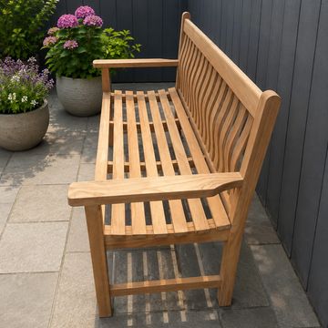Wooden bench on a patio next to flower pots against a dark fence.