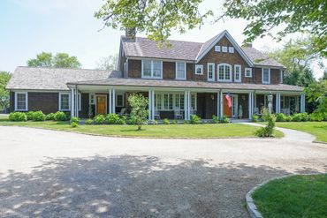 New England shingle style with a wrapped porch supported by classical columns 