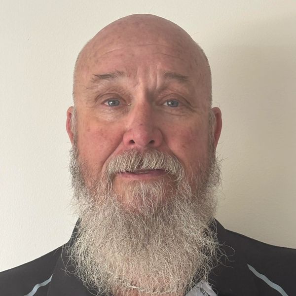 Portrait of a bald man with a long gray beard wearing a black shirt.
