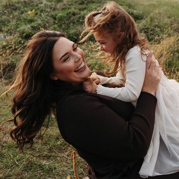 A joyful mother holding her happy daughter outdoors in a grassy field.