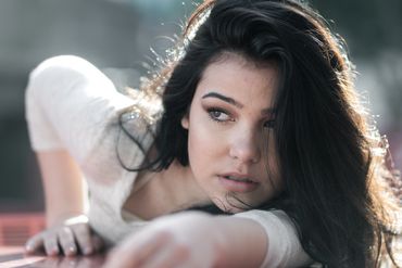 Young woman with dark hair reaching forward, looking sideways.