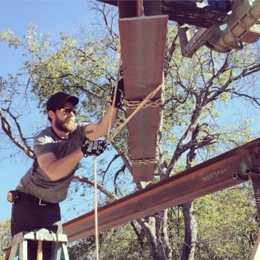 guy on a ladder trying to guide a steel beam into place