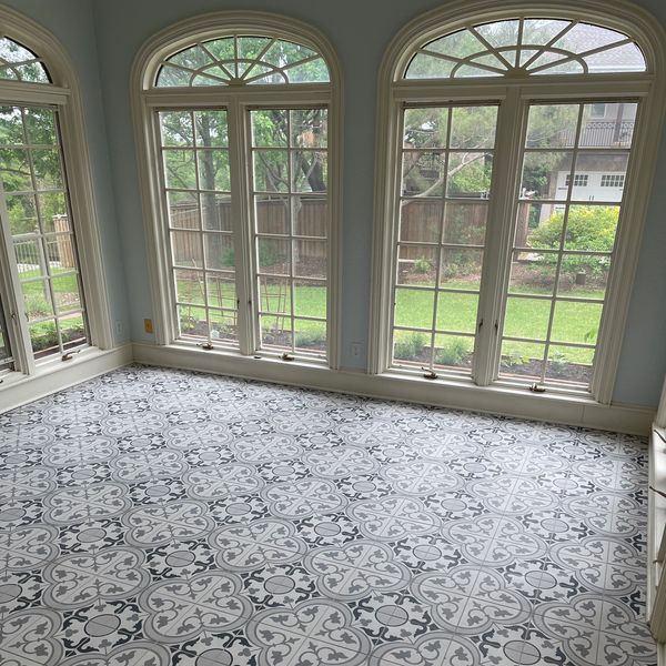Sunroom with patterned tile flooring and large windows overlooking a garden.
