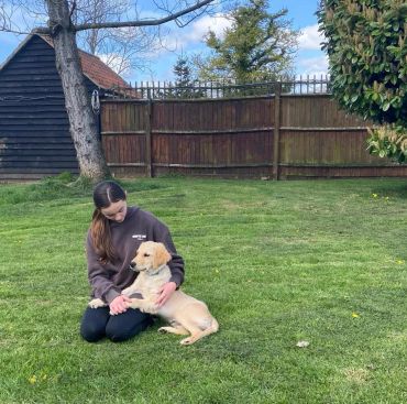 A woman sitting on grass petting a golden retriever puppy.