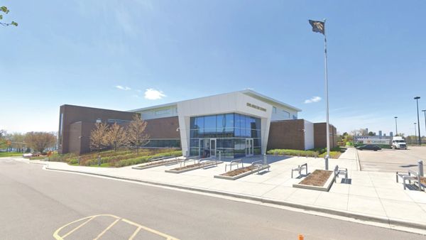 Modern public building with large glass entrance and flagpole under clear sky.