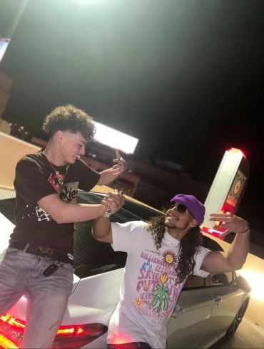 Two friends laughing and posing by a car at night.