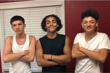 Three young men posing with crossed arms, smiling indoors.