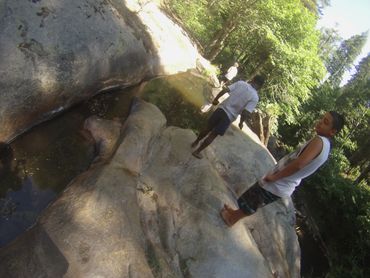 Two boys walking barefoot on rocky terrain near a small stream.