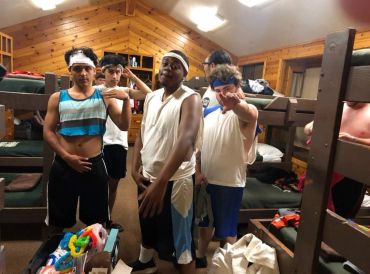 Five boys posing confidently in a wooden bunk room, dressed in sporty casual wear.