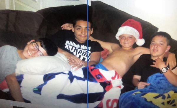 Four boys lounging on a couch, one wearing a Santa hat, covered with blankets.