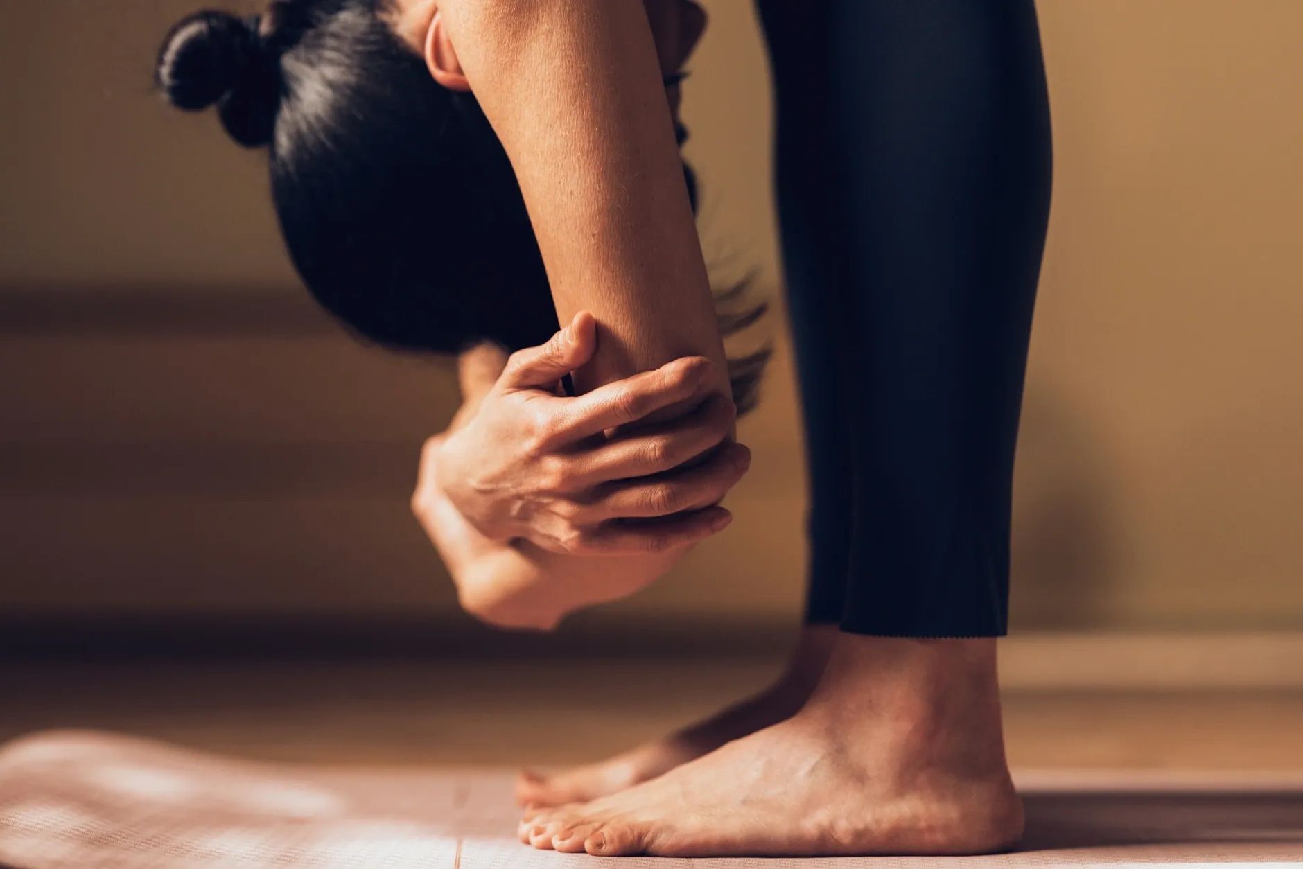 Person practicing a forward bend yoga pose on a mat indoors.