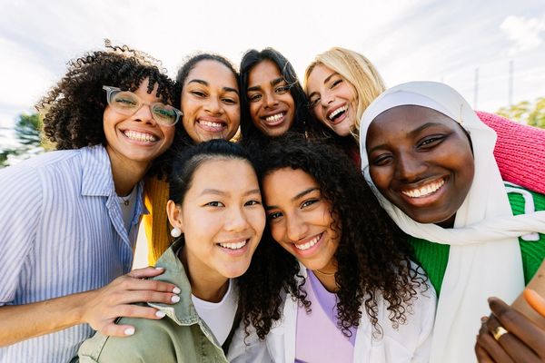 A diverse group of seven women smiling closely together outdoors.