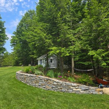 Stone wall with garden and trees behind a small house.
