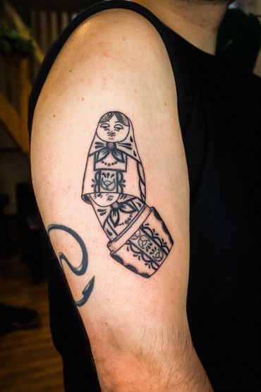 Tattoo of a broken Russian nesting doll on an arm.
