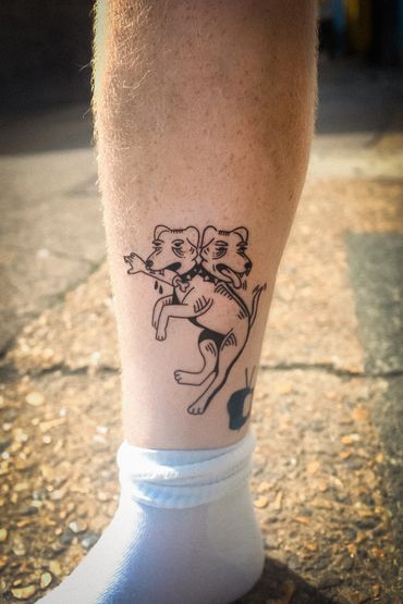 Tattoo of a two-headed dog with expressive faces on a person's calf.