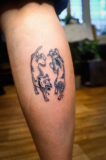Tattoo of a dog and a rabbit in a unique artistic style on a person's leg.