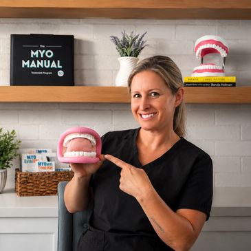 Woman in black scrubs holding a dental model and smiling.