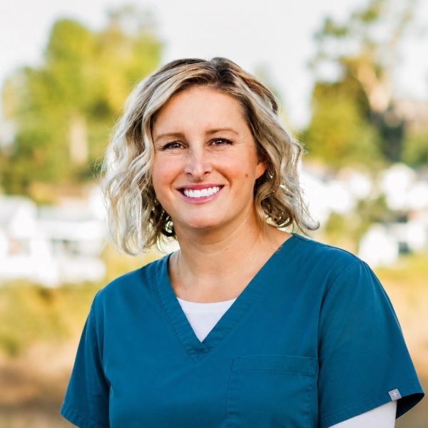Smiling woman in teal medical scrubs outdoors.