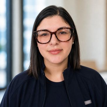 Woman with dark hair and large tortoiseshell glasses smiling gently.