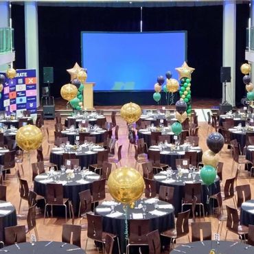 Large banquet hall decorated with gold, black, and green balloons.
